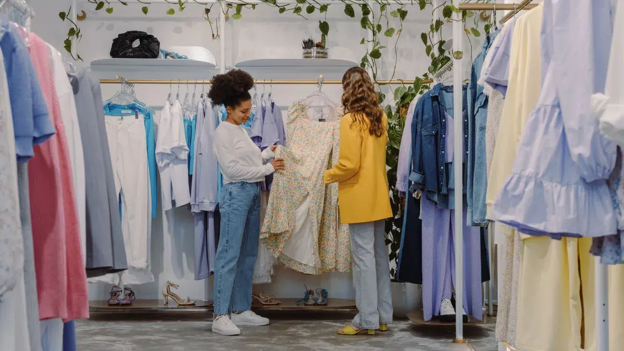 Dos personas eligen ropa en una tienda de moda con plantas decorativas.